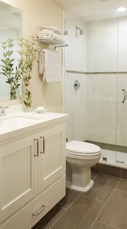 Small welcoming cream bathroom features a cream washstand placed on wood like floor tiles and fitted with a bottom drawer, satin nickel pulls, and a white quartz countertop holding a sink with a polished nickel faucet beneath a framless vanity mirror mounted to a cream wall. Cream Bathroom, Trendy Bathroom Tiles, Budget Bathroom Remodel, Narrow Bathroom, Bathroom Tub, Diy Bathroom Remodel, Bathroom Remodel Shower, Budget Bathroom, Trendy Bathroom