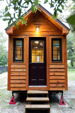 This is an identical tiny home, situated in a more traditional yard setting. Black door and window surrounds add contrast to the exterior. Tiny House Trailer Exterior, Micro House On Wheels, Stucco Tiny House, Camping House, Tiny House Exterior On Wheels, Diy Tiny House Plans, Mini Cabins, 2 Story Tiny House On Wheels, Mini Cabin