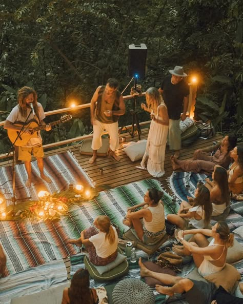 A warm and intimate gathering on a jungle villa terrace in Santa Teresa, Costa Rica. A musician plays an acoustic guitar surrounded by soft glowing lights and tropical greenery. Guests sit on colorful woven blankets and cushions, attentively enjoying the music while a few people stand and dance near the stage. The lush jungle surrounds the terrace, creating a serene, tropical ambiance. The atmosphere is relaxed, joyful, and connected, blending music, nature, and community into a magical moment. Costa Rica Santa Teresa, Intimate Concert, Costa Rica Retreat, Santa Teresa Costa Rica, Life Mood Board, Yoga Club, Jam Session, Bhakti Yoga, Events Photography