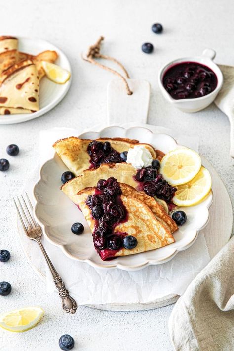 Three lemon crepes filled with blueberry compote and folded. The crepes are garnished with additional compote, whipped cream and lemon slices. This is a light, bright, magazine-style image. Lemon Crepes Filling, Ricotta Crepes, Blueberry Crepes, Lemon Crepes, Blueberry Sauce Recipe, Cake Waffles, Sweet Crepes Recipe, Crepe Ingredients, Morning Muffins