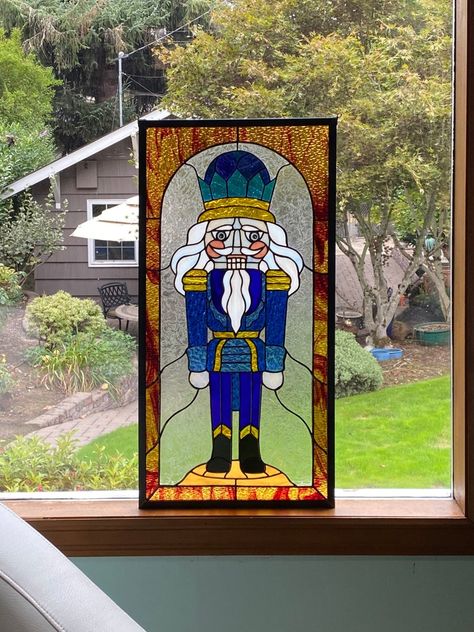 "A majestic nutcracker for your holiday season. This regal guy is dressed in a three-color blue wavy uniform capped with deeply textured gold accents. His silvery fox hair and beard are accented with an iridescent blue and gold crown. Framed in a gold and red candy swirled textured glass, this guy is perfect hanging in your window or displayed on a wall for your holiday delights. Sure to be a family heirloom in the years to come. DETAILS: This piece is finished at approximately 12.5\" by 25\". M Christmas Stained Glass, Fox Hair, Stained Glass Patterns Free, Stained Glass Ornaments, Large Window, Stained Glass Christmas, Iridescent Blue, Stained Glass Flowers, Stained Glass Diy