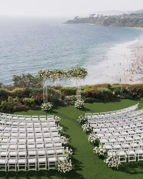 Say "I do" with the ocean as your backdrop in this breathtaking beachside wedding ceremony setup. With lush greenery, elegant white chairs, and a beautifully adorned floral arch, this setting offers the perfect combination of natural beauty and refined elegance. Ideal for couples looking to tie the knot in a serene and picturesque location by the White Chairs Wedding, Summer Wedding Venues, Ritz Carlton Laguna Niguel, Wedding Ceremony Setup, Natural Wedding Decor, Wedding Altar, Altar Ideas, Beachside Wedding, Ocean Backgrounds