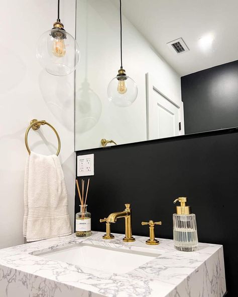 This powder room appears luxurious and modern with gold accets, a large mirror, and a marbled sink countertop. Contrasting against the black backdrop, the customized golden faucet pops out even more. Gold And Black Powder Room, Black Gold Half Bathroom, Black And Gold Powder Room, Powder Room Wallpaper Black And Gold, Gold Mirror Black Faucet, Room With Gold Accents, Luxurious Powder Room, Bold Wallpaper Bathroom Black And Gold, Room Wall Colors