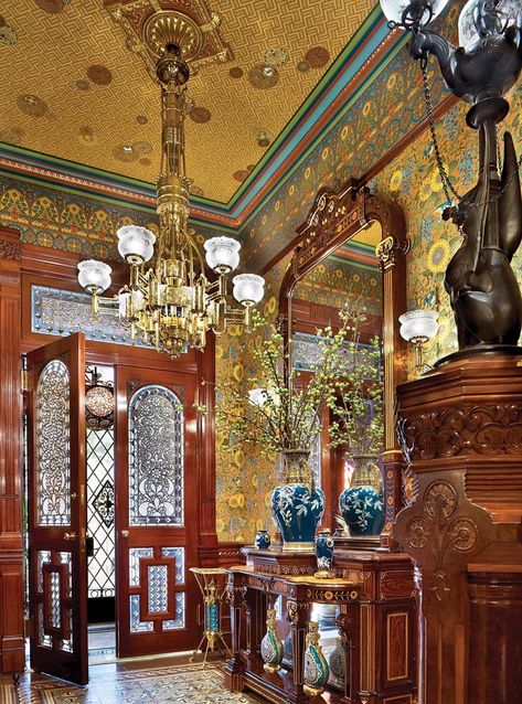 The foyer is entered via antique double doors that feature textured-glass panels and cabochon jewels. Colors of the original encaustic tile floor, made by Boch Freres, inspired the palette for the stairwell. Inspired by Bruce Talbert, David Scott Parker designed the sunflower wallpaper that continues up the stairwells, linking the floors. The rosewood mirror and gryphon newel lamp are attributed to Herter Brothers. Wallpaper Glass, Crystal Chandelier Dining Room, Victorian Rooms, Gold Chandeliers, Aesthetic Era, Victorian Home Interior, Victorian Interior, Victorian Interiors, Victorian Aesthetic