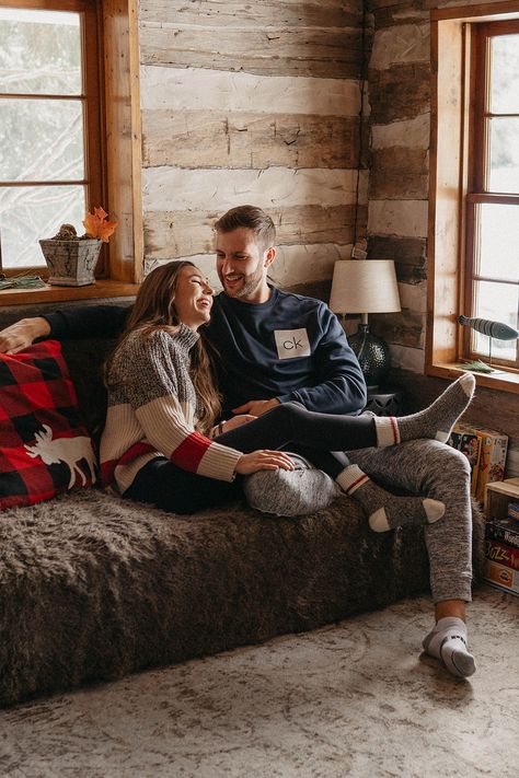 Couple sitting on the couch laughing together for their engagement photos Cozy Winter Engagement Shoot, Couple Cabin Photoshoot, Winter Cabin Photoshoot, Cabin Family Photos, Cozy Cabin Photoshoot, Cabin Family Photoshoot, Cabin Couple Pictures, Cabin Photoshoot Ideas, Cabin Engagement Photos