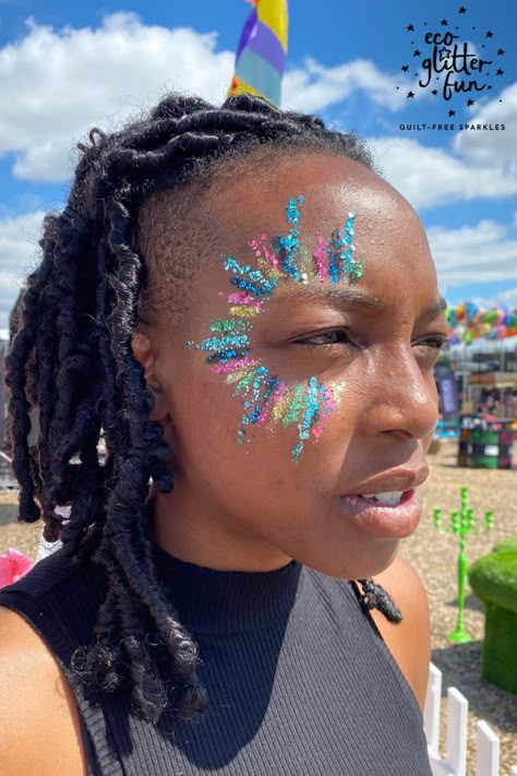 A lady wearing a star burst sun glitter design in blue, pink and gold. Looks like stripes around 1 eye Face Painting Glitter Festival, Summer Face Paint, Face Glitter Ideas, Make Up Festival, Festival Glitter Makeup, Glitter Face Makeup, Glitter Face Paint, Cheer Makeup, Festival Face Paint