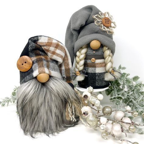 Gnomes can be the perfect embodiment of the rustic modern style. Their stoic grace just seems to fit with the contemporary aesthetic. This decorative gnome couple will brighten your winter holiday decor with their farmhouse charm and stylish plaid outfits. The gnomes are approximately 8" (20.5cm) tall, and 4" (10cm) around. They are made with a grey cotton-poly blend fabric stuffed with fill, fleece fabric, and wood noses. His stoic look is accomplished with a faux fur beard and mustache, while Country Gnomes, Homemade Gnomes, Diy Gnomes With Yarn Beards, Modern Farmhouse Christmas Decor, Stuffed Gnomes, Farmhouse Gnome, Winter Gnomes, Gnome Couple, Jute Flowers