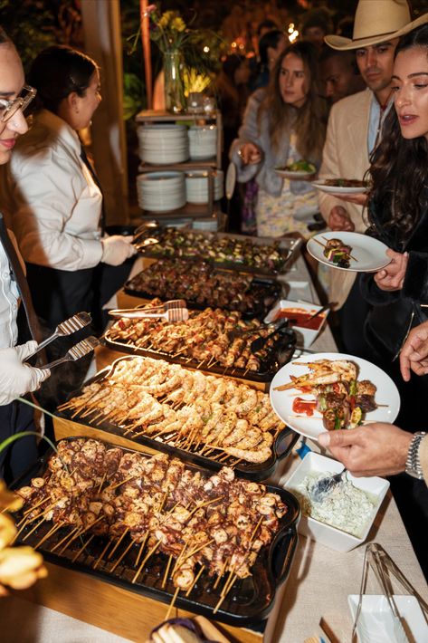 A group of people enjoying various food items from buffet stations. The individuals are seen socializing and having a good time while filling their plates with an assortment of appetizing dishes. The food stations are arranged in a visually appealing manner and showcase a wide range of cuisine options. Buffet Stations