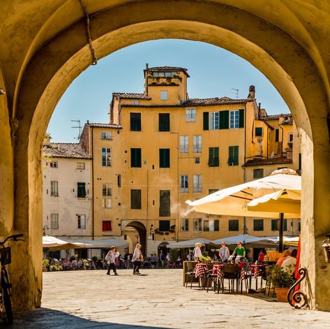 View through archway into Piazza dell'Anfiteatro.Piazza dell'Anfiteatro is a public square in the northeast quadrant of walled center of Lucca, region of Tuscany, Italy. The ring of buildings surrounding the square, follows the elliptical shape of the former second century Roman Amphitheater of Lucca. The square can be reached through four gateways located at the four vertices of the ellipse. A cross is carved into the central tile of the square with the arms pointing to the four gateways of t Italy Sketches, Lucca Italy, Toscana Italia, Public Square, Outdoor Cafe, Summer Getaway, Tuscany Italy, All Love, Lucca