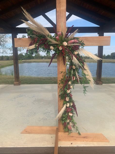 A combination of beatiful burgandy and blush florals combined with the trendy pampas grass softens the beatiful wooden wedding Cross for the picture perfect wedding Cross Swag Wedding, Boho Wedding Cross Decor, Diy Cross For Wedding, Cross Backdrop For Wedding, Decorated Cross For Wedding, Cross Floral Arrangements Wedding, Cross Arbor Wedding, Wedding Cross Altar, Wooden Cross Wedding