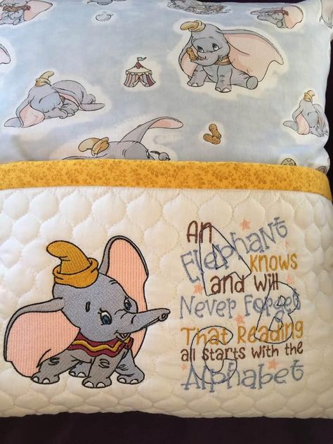 This is wonderful little cushion that will be loved by any child. It has very well elaborated design based on well known cartoon about little curious elephant. Center of this composition is Dumbo playing embroidery design. This sample is added by thematic inscription made with different fonts and printed fabric with figures of same elephant. All these elements look very nice together. Pillow Sayings, Book Pillows, Bernina Embroidery Machine, Elephant Cartoon, Embroidered Book, Bernina Embroidery, Photo Stitch, Flying Elephant, Book Pillow