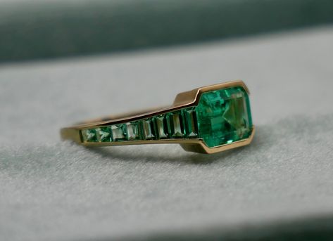 At the centerpiece of this lab grown Colombian emerald ring is a radiant 1.5 ct emerald, set east west to highlight its natural allure. Flanking it are calibre cut emeralds, each uniquely shaped to create a seamless gradient effect, making every ring truly one-of-a-kind. Set in luxurious 18K yellow gold, this ring exudes timeless charm. What makes it truly special? Calibre cut stones are individually shaped to fit precisely into the design, resulting in a mesmerizing display of color and brillia Nonbinary Engagement Ring, Emerald And Sapphire Ring, Emerald Ring Stack, Gem Stone Engagement Rings, Gold And Emerald Ring, Round Emerald Ring, Gem Cuts, Emerald Green Ring, Emerald Ring Design