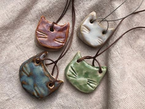 Handmade ceramic pendant necklace on faux leather adjustable cord.  Shaped as cat head. Different shades  to choose.  Can slightly vary in shape, size and colour as it is a handmade item. Introducing our handmade ceramic pendant necklace shaped as a charming cat head! This unique piece of jewelry is handcrafted with the utmost care and attention to detail. The pendant features a playful cat head design, perfectly capturing the playful spirit of these beloved animals. The pendant is glazed in a w Ceramic Cats, Ceramic Pendant Necklace, Colorful Cat, Cerámica Ideas, Pottery Handbuilding, Ceramic Cat, Ceramic Necklace, Cat Pendant, Pottery Crafts