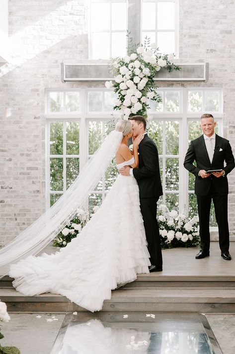 Bride and groom kissing during wedding ceremony in front of a cross with white roses and greenery installed on it Orchard Planning, Ground Florals, Indoor Roses, Elegant Wedding Ceremony, Peach Orchard, Orchard Wedding, Wedding Cross, Wedding Altars, Fairy Wedding