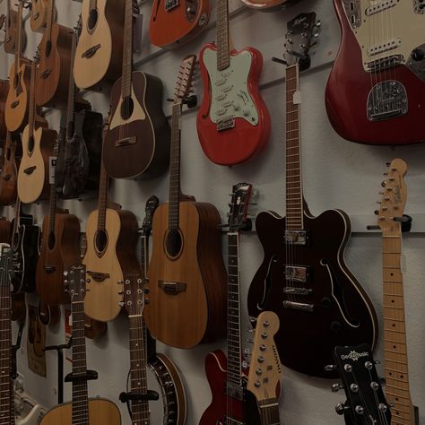 wall of guitars on white wall, guitars hanging from hooks Vintage Guitars Aesthetic, Guitar Asethic, Guitars On Wall Aesthetic, 70s Guitar Aesthetic, Guitar Vintage Aesthetic, Brown Guitar Aesthetic, Guitar Shop Aesthetic, Classic Guitar Aesthetic, Aesthetic Acoustic Guitar