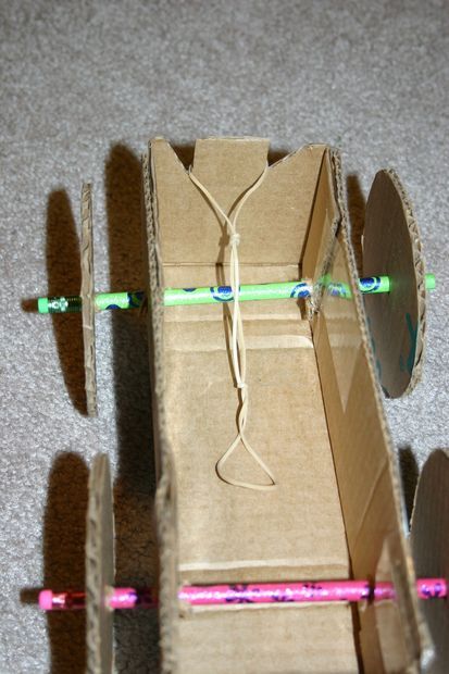 If you want to do something with those pesky cardboard shipping boxes, try making a toy car. You need rubber bands, cardboard, tape, glue, scissors and two pencils. Car Cardboard, Rubber Band Car, Cardboard Fireplace, Rubber Band Crafts, Cardboard Car, Cardboard Shipping Boxes, Cardboard Toys, Car Craft, Simple Machines