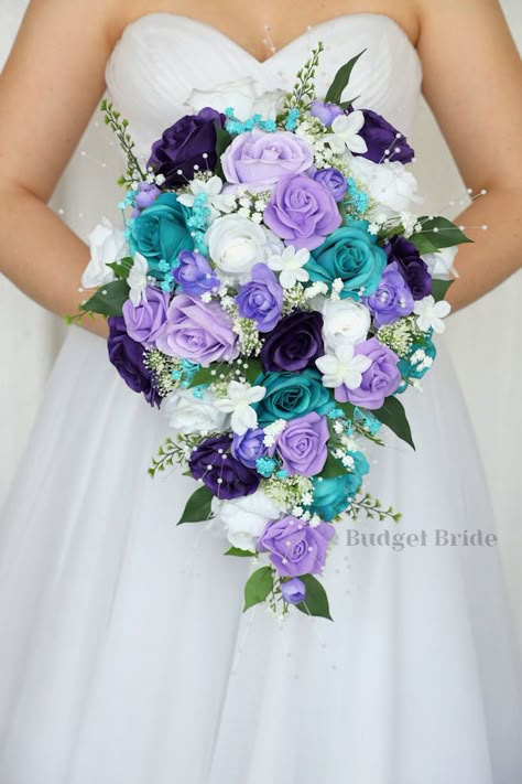 This lovely assortment of is bound to turn heads on your wedding day. This lovely cascading brides’ bouquet created with a mixture of royal purple, lavender, turquoise roses is an absolutely breathtaking arrangement for any bride to be, in any season. Bright greenery, turquoise babies breath and pearls complete the look and add a delicate realism to this beautiful bouquet. This bouquet is 10” wide, 18” long, and is crafted by our in-house florists without using a foam base to anchor the flowers Purple Blue Wedding Bouquets, Mint Green And Purple Wedding Theme, Purple And Aqua Wedding, Teal And Purple Wedding Decorations, Teal And Purple Wedding Theme, Purple Turquoise Wedding Reception, Stitch Wedding Ideas, Purple And Blue Bouquet, Turquoise And Purple Wedding