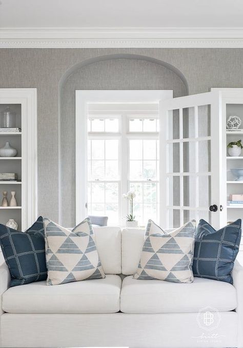 WHite and blue pillows accent a white linen couch placed in a white and gray living room in front of a glass-paneled door flanked by built-in alcove shelving. Pillows On White Couch, White Linen Couch, White And Gray Living Room, White Floating Desk, Grey Grasscloth Wallpaper, Ivory Sofa, Couch White, Alcove Shelving, Falling Leaf