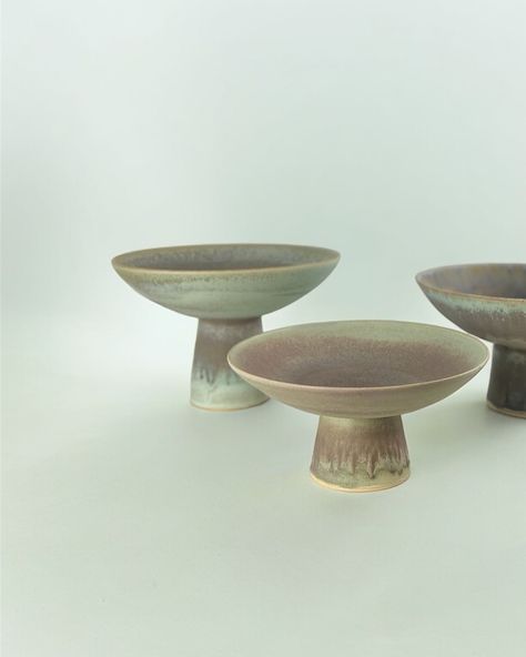 Envision a sunlit table draped in a soft linen cloth, bathed in natural light that dances across its surface. Elegant dishware is thoughtfully arranged, complemented by crystal glasses that catch the light, sparkling with promise, while tall, slender candles stand poised to add a warm, inviting glow. At the heart of this setting, three ceramic pedestal bowls take their place. One holds a vibrant array of seasonal fruits, their colors popping against the muted tones of the ceramics. Another c... Fruit In Season, Candle Stand, Linen Clothes, Natural Light, Ceramic Art, Color Pop, Table Settings, Sparkle, Bowl