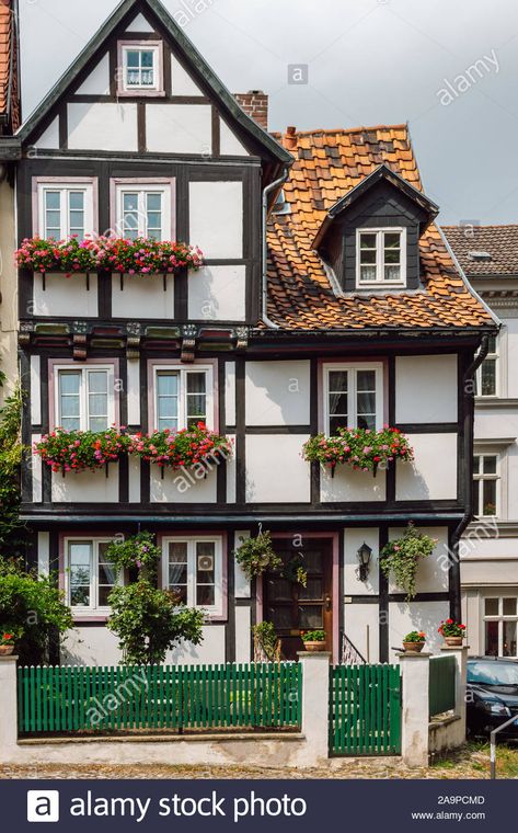 View of a traditional old German house with timber framing, windows decorated with red flowers and a green wooden fence in front of it, Quedlinburg. Stock Photo German Exterior House, German Houses Traditional, German Tudor House, Traditional German House, German House Aesthetic, German Architecture Traditional, German Townhouse, German House Exterior, Germanic Architecture