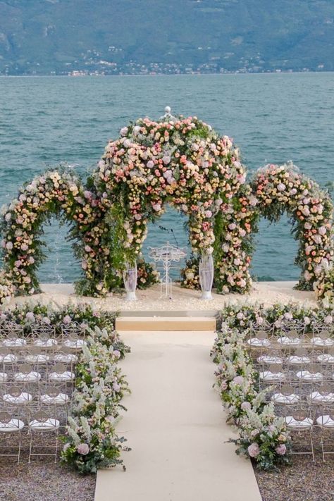 This stunning lakeside wedding ceremony setup features a breathtaking floral arch adorned with soft pinks, whites, and greenery, perfectly complementing the serene backdrop of the water. The elegant seating arrangement and floral-lined aisle create an intimate and romantic atmosphere, making it an ideal inspiration for an outdoor wedding by the water. #LakesideWedding #WeddingCeremony #OutdoorWedding Altar Design Wedding, Lake View Wedding, Glamorous Wedding Venue, Wedding By The Water, Lakeside Wedding Ceremony, Wedding Aisles, Decoration Engagement, Wedding Ceremony Setup, Wedding Forest