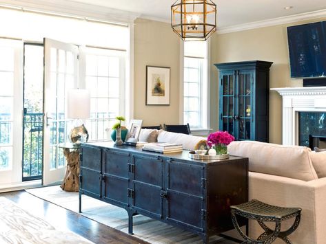 This neutral condo living room features an antique sideboard that serves as a console table behind an off-white sofa. A chandelier with a metal geometric pattern provides light for the space, and a dark glass-front cabinet provides storage and display space. Behind Sofa, Table Behind Couch, Condo Living Room, Behind Couch, Storage Inspiration, Industrial Livingroom, Traditional Interior Design, Couch Decor, Transitional Living