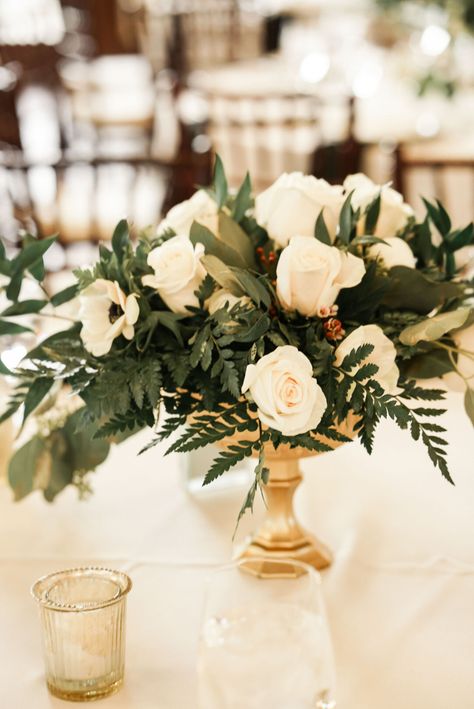 White Roses, White Ranunculus, White Anemone, White Waxflower, Silver Dollar Eucalyptus, Seeded Eucalyptus, Leatherleaf Fern, Italian Ruscus. Gold Pedestal Vase. Gold Pedestal Centerpiece, White Rose And Eucalyptus Centerpiece, White Flowers With Gold Accents, Gold Vase White Flower Centerpieces, White Green Gold Flower Arrangements, Pedestal Vase Centerpiece, White Floral Centerpiece In Gold Vase, White Florals In Gold Compote Vase Wedding Centerpiece, Gold Table Centerpieces