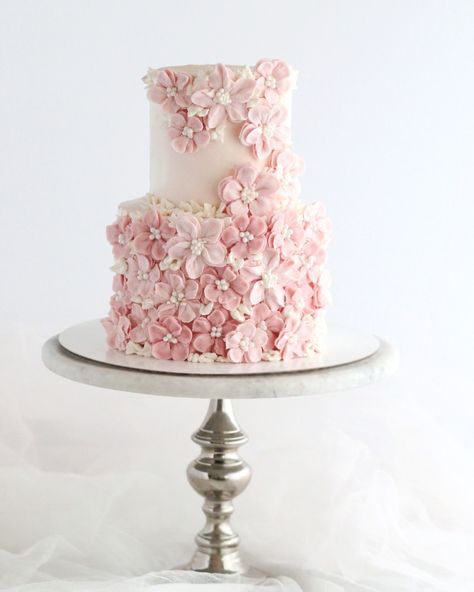 A two-tier cake adorned with delicate pink buttercream flowers, each with a pearl center. The bottom tier is fully enveloped in flowers and ivory leaves, creating a textured floral canvas. The top tier has a cascade of flowers flowing down one side. 2 Tier Pink Cake, Pink Cake With Flowers, Pink Buttercream, Two Tier Cake, 2 Tier Cake, Cake With Flowers, Cake White, Tier Cake, Buttercream Flowers