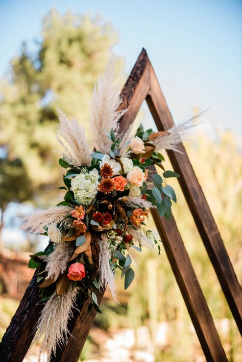 Modern triangle wedding ceremony arch with boho inspired wedding flowers in burnt ochre and blush. Fall wedding decor Wedding 2023 Decor, Fall Triangle Arch, Boho Wedding Triangle Arch, Boho Floral Arch Wedding, Fall Wedding Triangle Arch, Boho Arbor Floral Arrangement, Boho Isle Wedding, November Wedding Arch, Diy Boho Wedding Arch Flowers