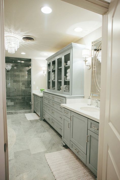 French master bathroom features separate gray washstands topped with white quartz under rectangular Venetian mirrors flanking a gray glass-front linen cabinet stacked over dresser like storage drawers atop a gray staggered tiled floor. Long Narrow Bathroom, Woods House, French Bathroom, Georgian Colonial, Magnolia Farms, Narrow Bathroom, Bathroom Chic, Bathroom Images, Master Bath Ideas