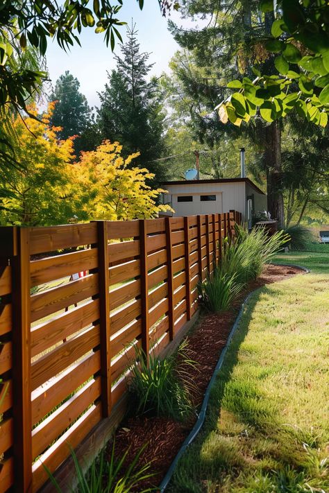 A wooden fence lines a garden path, with greenery and a variety of trees in the background on a sunny day. A small house is visible beyond the fence. Inexpensive Backyard Fence Ideas, Home Made Fence Ideas, Country Privacy Fence Ideas, Front Privacy Fence, Easy Cheap Fence Ideas, Vertical Privacy Fence Ideas, Wood Fence Ideas Backyards, Fence In Front Of House, Fence Around Tree