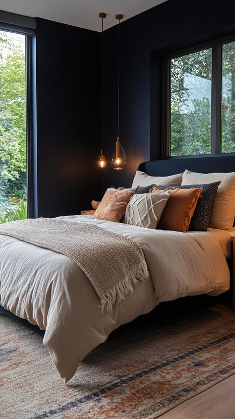 A cozy modern bedroom featuring a dark navy accent wall, a plush king-size bed with stylish bedding, natural wood bedside tables, and soft ambient lighting. Floor-to-ceiling windows frame a serene garden view. Dark Navy Accent Wall, Navy And Rust Bedroom, Cozy Modern Bedroom Ideas, Natural Wood Bedside Table, Navy Accent Wall, Cozy Modern Bedroom, Tan Bedding, Wood Bedside Tables, Navy Accent Walls