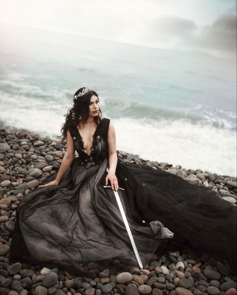 A dark hair princess sitting on the rocky beach holding her sword by her hip with the waves crashing in the background beach photoshoot by photographer Natasha Sachi Fantasy Princess Photography, Dark Hair Princess, Fantasy Photoshoot Ideas, Unseen Photography, Warrior Photoshoot, Princess Aesthetic Dark, Warrior Princess Aesthetic, Fantasy Moodboard, Gloomy Beach