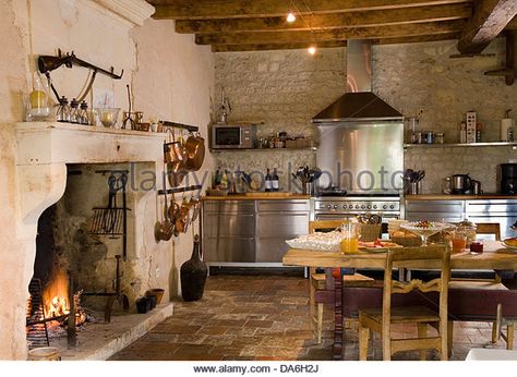 Lit fire in fireplace in country kitchen with rustic wooden table and chairs stainless steel fitted units - Stock Image Country Kitchen With Fireplace, Cooking Fireplace In Kitchen, Stone Fireplace In Kitchen, Fireplace Kitchen Ideas, Kitchen Fireplace Cooking, Kitchen Fireplace Ideas, Fire In Fireplace, Fireplace In Kitchen, Country Goth