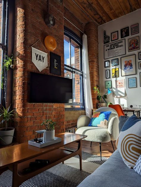 Strong light and shadow against a double-height gallery wall in a loft apartment decorated with colourful homewares and vintage furniture Mill Building Apartment Decor, Boston Apartment Aesthetic Living Room, Brick Apartment Living Room, Maximalist New York Apartment, Brick Wall Apartment Decor, Loft Flat Interior Design, Brick Wall Room Decor, Exposed Brick Apartment Aesthetic, Brick Loft Apartment Decor