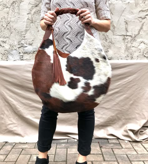 "Add lining to any of our bags https://www.etsy.com/listing/891051352 Unique cowhide leather hobo bag, with brown braided strap and two tassels (included) Measurements- 19\" wide x 19\" high 14\" high in the middle This is a large size, slouchy, handmade leather bag, with feminine design and a braided black strap. Made with soft hair on leather leather. The bag is great for your daily essentials, perfect for everyday use, or for a special occasion. It can hold your school items, groceries, walle Modern Bags Design, Cowhide Bags Handbags, Hair On Leather Bags, Cow Print Bag, Leather Hobo Bags, Bag Styles, Cowhide Purse, Leather Hip Bag, Slouchy Bag