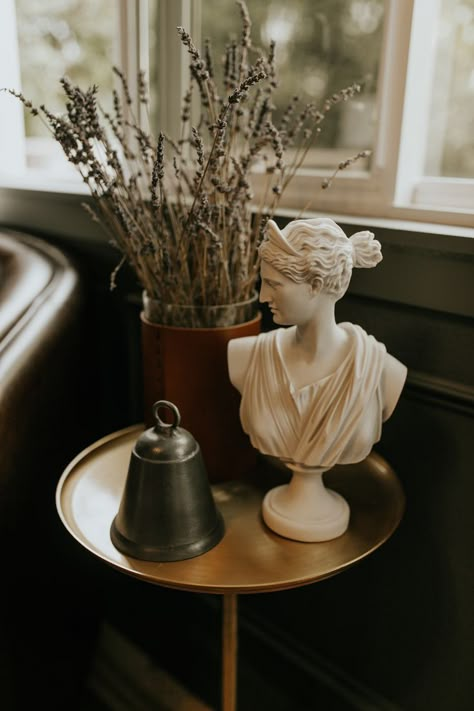 Bust sculpture, silver bell, dried lavendar, leather wrapped vase, gold side table Roman Bust Decor, Bust Statue Decor, Small Sculpture Ideas, Artifacts For Home Decor, Roman Decor, Bust Decor, Roman Busts, Greek Decor, Gold Side Table