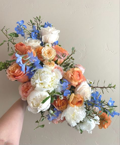 Peach and blue bridal bouquet by Utah based florist Maree Floral Co. This bouquet features peach ranunculus, peach David Austen Juliet garden roses, light blue delphinium, peach roses, white roses, eucalyptus. The crowning flower of this bouquet are some lovely fragrant white peonies. Peach And Blue Cascading Bouquet, Blue Peach Bouquet, Peach And Blue Flower Arrangements, Blue And Orange Flower Arrangements, Blue And Peach Bouquet, Blue And Orange Bouquet, Juliet Rose Bouquet, Blush Wedding Flowers Centerpiece, Peach And Blue Wedding