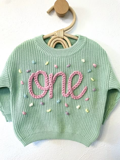 Our custom hand embroidered name sweaters are sure to look adorable on the sweet little one in your life!  Give them as gifts for baby showers, name announcements, first birthday's, Xmas gifts, and more!  Sweaters are a chunky knit and an oversized fit to wear as your baby grows.  These are perfect to wear in the fall, winter, or spring. Choose the color and size of your sweater in the above drop down.  Choose your name/word color and confetti color, then insert in the personalization area. Care Custom Knit Sweater, One Embroidered Sweater, Embroidery On Clothes Diy, Embroidery Kids Clothes, Hand Embroidery Sweater, Embroidered Name Sweater, Baby Name Sweater, Hand Embroidered Name, Birthday Sweater