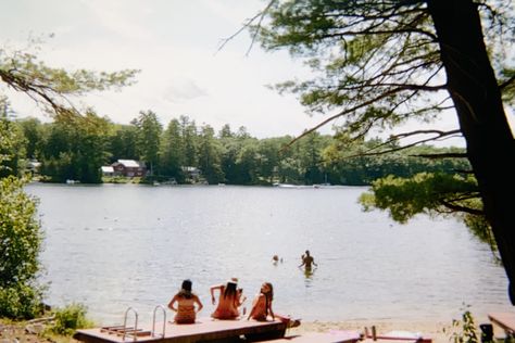 Image is of a lake. There are a few people sitting by the lake on beached docks and a few people in the water. Camp Lake Aesthetic, 1980s Summer Camp Aesthetic, Vintage Summer Camp Aesthetic, 80s Summer Camp Aesthetic, American Summer Aesthetic, Lake Day Aesthetic, Lake Summer Aesthetic, Vintage Summer Camp, American Summer Camp