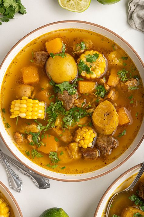 Sancocho is a soup with origins in the Caribbean, known for its rich flavors thanks to a blend of stewed beef, chicken, root veggies, and corn. This Puerto Rican version is loaded with flavor thanks to sofrito, sazon, and adobo seasoning, plus lots of fresh veggies like green plantain, yams, potatoes, and squash. Sancocho Recipe Puerto Rican, Sancocho Puerto Rican, Puerto Rican Beef Stew, Sancocho Recipe, Stewed Beef, Spanish Soup, Veggie Stew, Beef And Potato Stew, Yam Or Sweet Potato