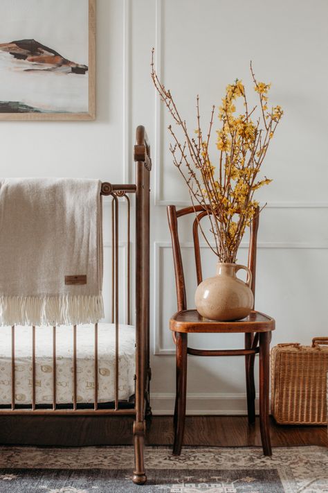 Vignette featuring antique gold iron crib against a white wall with picture frame molding. Yellow flower branches sit on top of a vintage bistro chair Picture Frame Accent Wall, Iron Crib Nursery, White Crib Nursery, Dark Wood Nursery, Iron Crib, Beige Nursery, Wood Crib, Neutral Crib, Changing Pad Covers