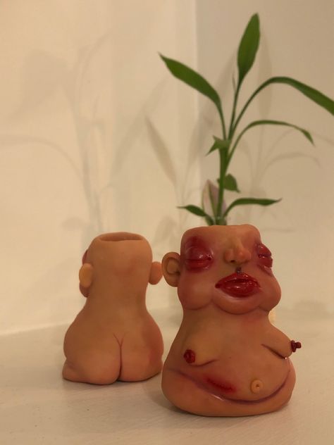 In the foreground, a clay blobby dude with olive tan skin, maroon eyeshadow and puffy red under eyes. Voluptuous red lips, and a scar on the lower stomach simulating a recently removed appendix. Saggy exposed boobs, and pudgy stomach. A tall leafy plant appears to be coming from its head. In the background, a figure of similar height and skin tone, facing away from the camera to show its buttcrack ~ simulating a mirror image.  

Plain white surroundings and warm light. Lighter Holder Clay, Clay Lighter Holder, Clay Lighter, Clay Diys, Lighter Holder, Candle Pot, Light Clay, Clay Diy Projects, Loving You