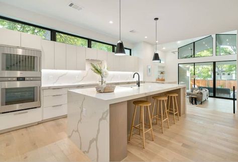 The pair of hanging pendant lights over the marble kitchen island is augmented by the backlight underneath the white wall-mounted cabinets over the kitchen peninsula. The brightness is complemented by the white walls and hardwood flooring. Simple Kitchen Tiles, Basic Kitchen Design, Modern Scandi Kitchen, Modern Scandinavian Kitchen, Marble Kitchen Island, Scandi Kitchen, Scandinavian Kitchen Design, Kitchen Tiles Design, Beige Kitchen