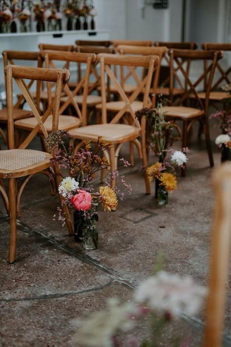 Small floral arrangements in bright colours with retro vibe sit beside wooden chairs lining the aisle | Wedding Aisle Centerpieces, Flower Vases Down Aisle, Affordable Wedding Aisle Decorations, Top Of Aisle Decor, Inexpensive Aisle Decorations Wedding, Wild Flower Wedding Chairs, Chair Decor Ideas Wedding, Simple Isle Decoration, Minimal Isle Decor