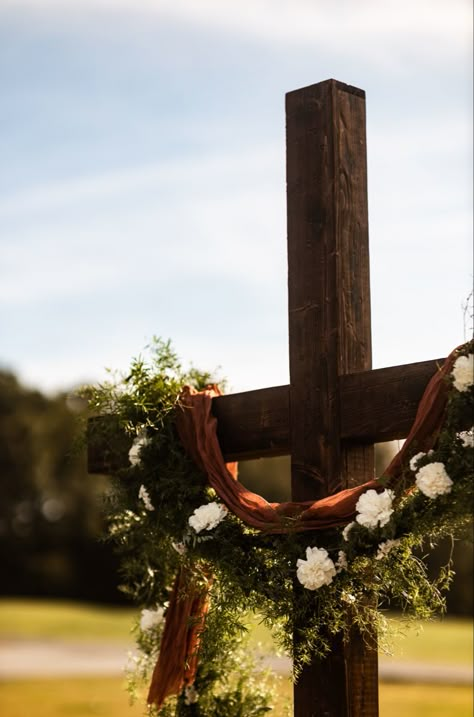 Beautiful cross with terracotta cheese cloth, greenery garland and white floral accents Cross Arbor Wedding Fall, Wedding Cross Altar Outdoor Ceremony, Cross Arbor Wedding, Cross Alters For Weddings, Cross Wedding Alter, Wedding Cross Decor, Cross For Wedding Ceremony, Wedding Alter Decor, Cross Wedding Backdrop