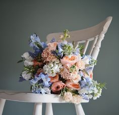 A spring bridal bouquet of Peaches, Coral & Pale Blue created by Eden Blooms Florist for Cain Manor Bride. Made from Rannunculus, Stocks, Rosemary, Delphinium, Sweet Pea, David Austin 'Juliet' Rose, Muscari & Olive Foliage. Image by Eden Blooms Florist. Wedding Bouquets Blue, Modern Wedding Flowers Arrangements, Cain Manor, Olive Foliage, Spring Bridal Bouquet, Juliet Rose, Early Spring Wedding, Bridal Bouquet Spring, Peach Wedding Flowers