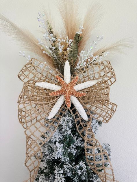 "This starfish tree topper will be the perfect addition to your family's beach holiday tree. Made with white 7-8\" starfish, sugar (orange) starfish, burlap net ribbon bow with 24\" tails (can be cut shorter), artificial pampas (does not shed), white glitter grass, and faux green seagrass.  This is a one-sided (180 degrees) tree topper. Need it to be double-sided? Order two! :) This topper will stick down into the top of your tree and  be able to be tied to the base of your tree with chenille st Seashell Tree Topper, Coastal Christmas Tree Toppers, Christmas Ocean Theme, Starfish Tree Topper Diy, Nautical Tree Topper, Beach Theme Tree, Nautical Christmas Tree Topper, Coastal Christmas Tree Topper, Coastal Tree Topper