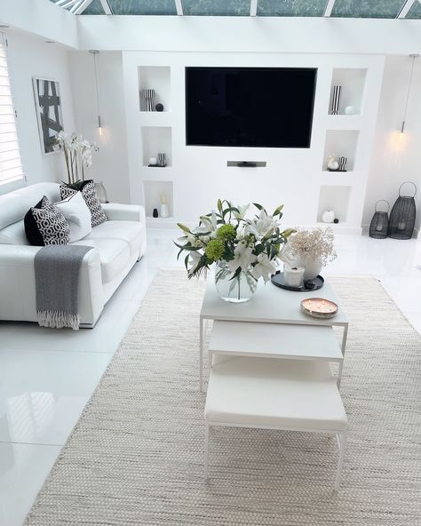 White scandi style front living room. White tiled floor and walls with a white leather sofa and arm chair with black details. Lots of vases flowers, candles and book decor
White lilies 
Blankets 
Abstract artwork on the walls 
TV media wall 
Stacked coffee table
Black lanterns Built In Media Wall, Tv Media Wall, Style Living Room, Tv Media, Media Wall, Modern Tv, Scandi Style, Garden Room, Coffee Table