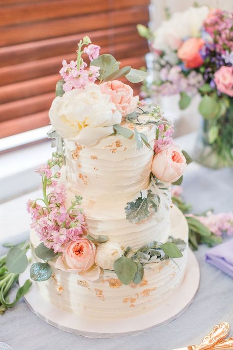 Spring wedding cake at reception. White 3 tiered buttercream with soft pastel colored flowers on the frosting. Bridgerton Pastel Wedding Theme, White Wedding Cake Pink Flowers, Aesthetic Wedding Cake Korean, Spring Pastel Wedding Cake, Spring Themed Wedding Cake, Pastel And Greenery Wedding, Peonies Wedding Cake, Pastel Wedding Flowers Table, Elegant Floral Wedding Cake